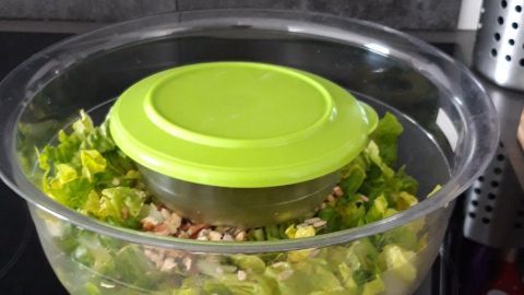 Ein transparentes Glas mit frischem Salat und einem grünen Deckel steht auf einem Herd, bereit zum sicheren Transport.