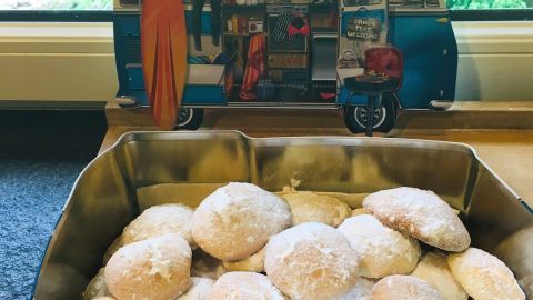 Zarte Biscotti al limone liegen in einer goldenen Schale, während ein buntes Kastenwagen-Motiv im Hintergrund sichtbar ist.