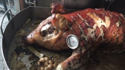 Ein Spanferkel liegt in einem Lehmbackofen, perfekt gegart und knusprig, umgeben von aromatischem Gemüse.