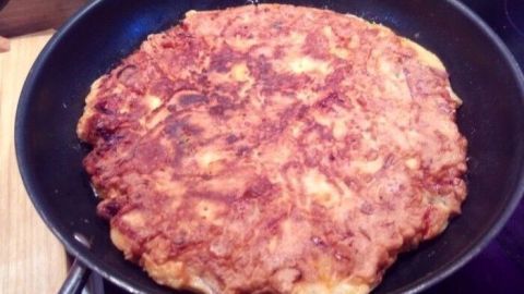 Ein goldbrauner Pfannkuchen wird in einer schwarzen Pfanne gebraten, umgeben von einer modernen Küchenumgebung.