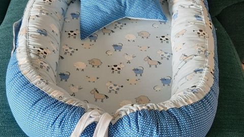 Ein Babynest in sanften Blautönen liegt auf einem grünen Sofa, dekoriert mit einem Sternkissen und kleinen Stoffsternen.