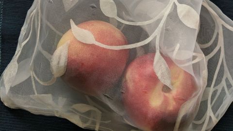 Ein netzartiger Beutel aus Gardinen-Resten hält mehrere Äpfel und liegt auf einem blauen Untergrund.