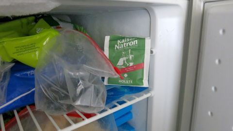 Natron kann das Vereisen des Gefrierfachs verhindern! Ein offenes Päckchen im Gefrierfach nimmt Feuchtigkeit auf und reduziert Eisbildung nachhaltig. Probiere diesen einfachen Trick, um Vereisung zu vermeiden. Natronbeutel im Gefrierfach hält Lebensmittel frisch; umgeben von Tüten mit Tiefkühlware. Text: "Kaiser Natron HOLSTE".
