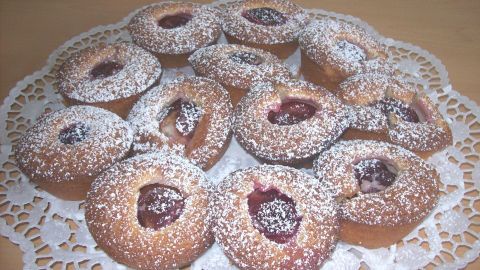 Saftige Pflaumen-Muffins mit Marzipan liegen auf einer dekorativen Serviette, mit Puderzucker bestäubt.