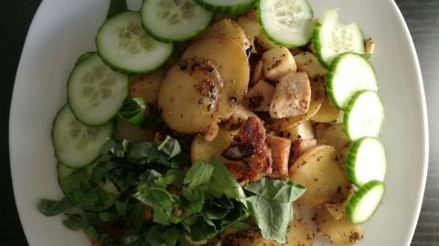Bratkartoffeln liegen goldbraun auf dem Teller, umgeben von Gurkenscheiben und frischem grünen Salat.