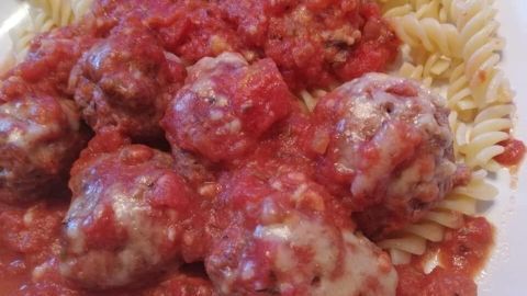 Saftige Hackbällchen liegen in einer roten Tomatensoße und umgeben von gedrehten Pasta auf einem Teller.