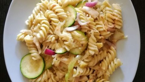 Fusilli mit Meeresfrüchten auf einem Teller, umgeben von frischem Gemüse, strahlt mediterranen Genuss aus.