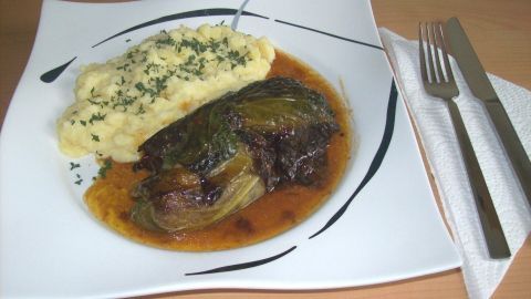 Rostbratwurst umhüllt von Wirsing, serviert mit cremigem Kartoffelbrei auf einem eleganten weißen Teller.