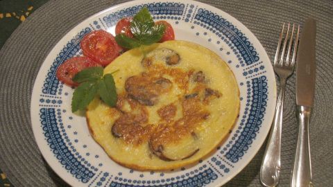 Kleine gefüllte Pfannkuchen mit Champignons liegen auf einem dekorativen Teller, umgeben von frischen Tomaten und Salat.