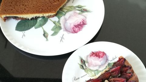Ein Stück Zwetschgendatschi liegt auf einem blumigen Teller, während die gesamte Torte auf einem größeren Teller sichtbar ist.