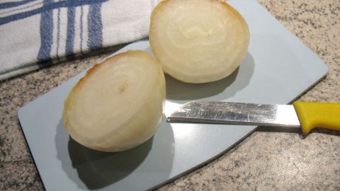 Auf einem Schneidebrett liegt eine halbierte Zwiebel, während ein Messer daneben bereitliegt, um sie weiter vorzubereiten.