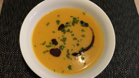 Eine cremige Kürbissuppe mit Kokosmilch und Birne, garniert mit Kräutern und einem Schuss Balsamico, serviert in einer weißen Schüssel.