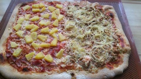 Ein großer Pizzaboden ist mit fruchtigen Ananasstücken und einer würzigen Käsemischung belegt, gebacken auf einem Blech.