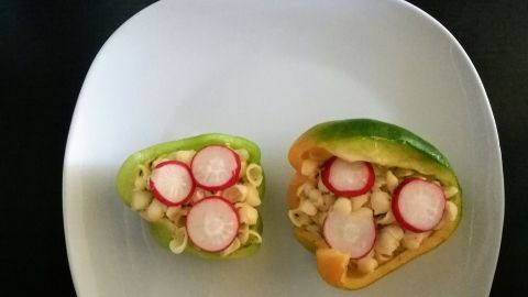 Gefüllte Paprika zeigen Nudeln und Radieschen, angerichtet auf einem weißen Teller, umgeben von einem dunklen Hintergrund.