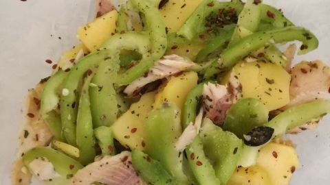 Ein bunter Kartoffelsalat aus gewürfelten Kartoffeln und grüner Paprika liegt auf weißem Papier, angereichert mit Räucherforelle.