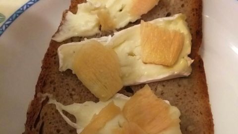 Eine Scheibe Vollkornbrot ist mit cremigem Käse und mildem, eingelegtem Ingwer belegt, serviert auf traditionellem Porzellanteller.