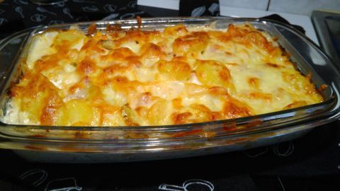 Ein köstliches Kartoffel-Kürbis-Gratin, goldbraun überbacken, steht heiß aus dem Ofen auf einer dunklen Arbeitsfläche.
