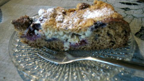 Eine Beerentorte mit Cashew-Streuseln liegt auf einem gläsernen Teller, während ein Löffel daneben bereitsteht.