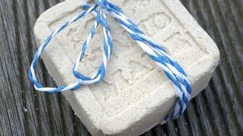 Ein festes Shampoo liegt auf einer Holzoberfläche, mit blauer Schnur dekorativ umwickelt, bereit zur Verwendung.