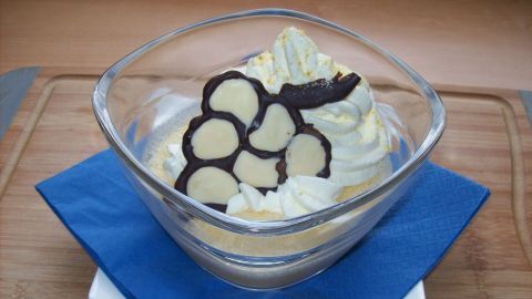 Vor dem Servieren schlägt man die Sahne, füllt sie in einen Spritzbeutel und dekoriert damit die Creme. Etwas Zitronenabrieb wird über die Sahnehaube gestreut.