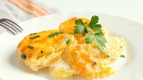 Ein goldbraun gebackenes Kartoffelgratin liegt auf einem weißen Teller, verziert mit frischer Petersilie, im Hintergrund ein schlichtes Tischtuch.