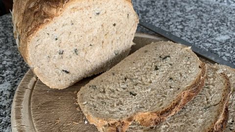 Ein Laib Brot mit Kürbiskernen liegt auf einem Holzbrett, während einige Scheiben davon geschnitten und daneben platziert sind.