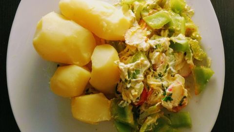 Gekochte Kartoffeln liegen neben einem bunten Gemüse-Dip aus Frischkäse und Joghurt auf einem weißen Teller.