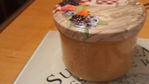 Ein Glas mit dekorativem Holzdeckel steht auf einem Tisch, umgeben von einer modernen Küchenoberfläche, wahrscheinlich gefüllt mit Bananen-Birnen-Marmelade.