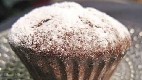 Ein Marzipan-Muffin liegt auf einem dekorativen Teller und wird von feinem Puderzucker bestreut, umgeben von einem gemütlichen Ambiente.