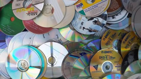 Überzählige CDs liegen bunt gemischt auf einem Tisch, reflektierend im Licht, und warten auf eine neue Verwendung.