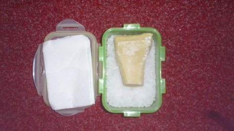 Parmesan über Jahre haltbar machen, geht das denn überhaupt? Ja, mit diesem Tipp, gelingt das sehr gut. Ein Stück Parmesan liegt in einem grünen Behälter, umgeben von Salz, zur Langzeitlagerung.