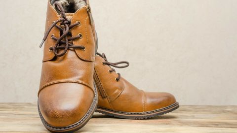 Braune Lederschuhe stehen auf einem Holzuntergrund und warten darauf, mit weißem Speck gepflegt zu werden.