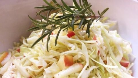 Frischer Chinakohlsalat in einer Schüssel, garnierte mit Apfelstücken und einem Zweig Rosmarin, serviert in einer gemütlichen Küche.