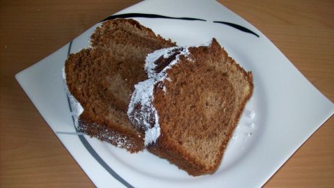 Auf einem weißen Teller liegen zwei Scheiben eines winterlichen Gewürzkuchens, leicht mit Puderzucker bestreut.