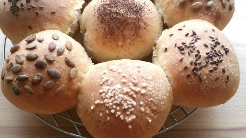 Zehn frisch gebackene Brötchen stehen in Form einer Blume auf einem Kuchengitter. Sie haben verschiedene Toppings.