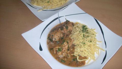 Saftige Putenrollen liegen neben Spätzle auf einem weißen Teller, angerichtet auf einem Holztisch in einer einfachen Küche.