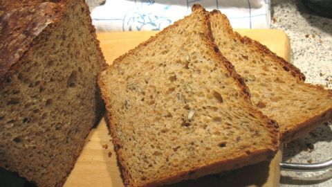 Ein frisch gebackenes Dinkel-Vollkornbrot auf einem Holzbrett, mit ein paar aufgeschnittenen Scheiben in einer Küche.