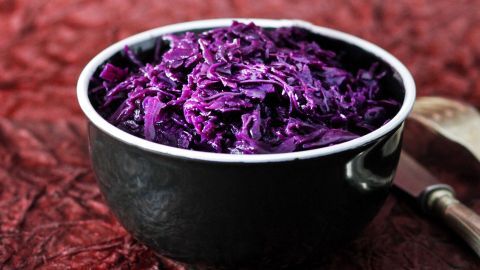 Dunkelblaues Rotkohl aus dem Glas wird in einer Schüssel präsentiert, umgeben von einem roten, strukturierten Hintergrund.