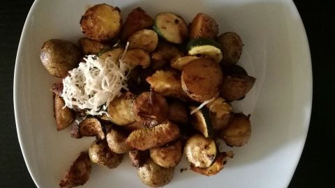 Bratkartoffeln liegen auf einem Teller, goldbraun und knusprig, umgeben von Zucchini und Meerrettich.