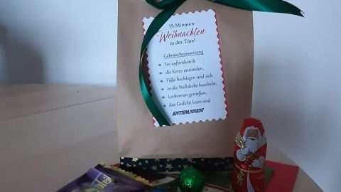 Eine braune Tüte mit grüner Schleife steht auf einem Tisch, gefüllt mit weihnachtlichen Süßigkeiten und einer Liste für 15 Minuten-Weihnachten.