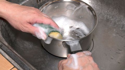 Ein Topf wird mit einem Schwamm und Seife im Spülbecken gereinigt, um angebrannte Rückstände zu entfernen.
