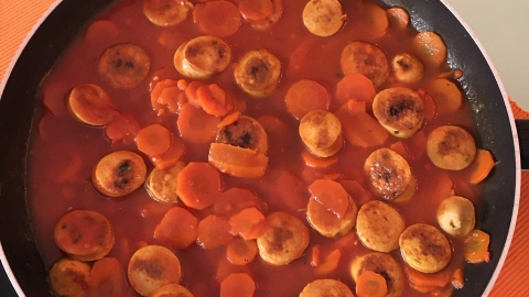 Schnelles Bratwurstgulasch mit Karotten köchelt in einer Pfanne auf einem orangefarbenen Platzset, voller leuchtender Karottenscheiben.