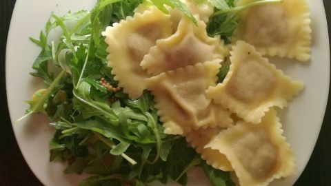 Auf einem weißen Teller liegen Ravioli mit Hackfleischfüllung, umgeben von frischem Rucola.