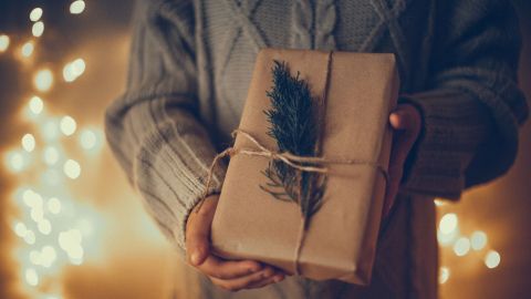 Ein sorgfältig verpacktes Geschenk mit Naturmaterialien wird von einer Person in einem warmen, weihnachtlichen Umfeld gehalten.