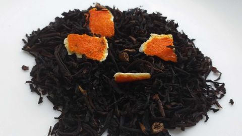 Schwarztee liegt mit kleinen Orangenschalenstücken auf einem weißen Teller, bereit zu einem aromatischen Genuss.