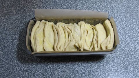 Ein Kasten mit unbacken gefalteten Teigstücken für Weihnachtsgebäck liegt auf einer grauen Arbeitsplatte.