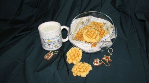 Zwei knusprige Mürbchen liegen neben einer Tasse Milch auf einem dunklen Tuch, umgeben von goldenen Ohrringen.