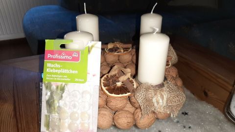 Ein Adventskranz mit weißen Kerzen steht dekorativ auf einem Tisch, umgeben von Naturmaterialien und einem Paket für Kerzenhalter.