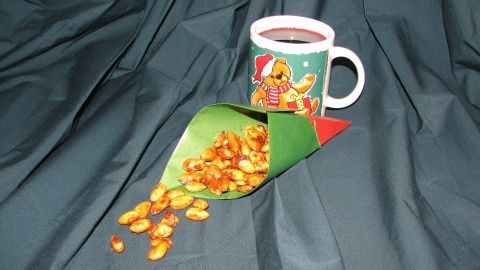 Eine Tasse mit heißem Muskatkaffee steht neben einer grünen Papiertüte, aus der gebrannte Mandeln fallen.