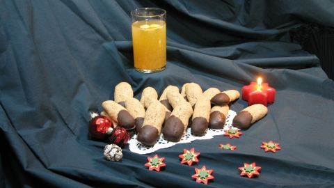 Zimtstangen liegen neben Weihnachtsschmuck und einem Glas heißem Ingwer-Apfelsaft auf einem dunklen Tuch, umgeben von festlicher Dekoration.